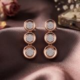 A pair of rose gold drop earrings with three stacked circular charms, each featuring a detailed DIAMOND CLUSTER.