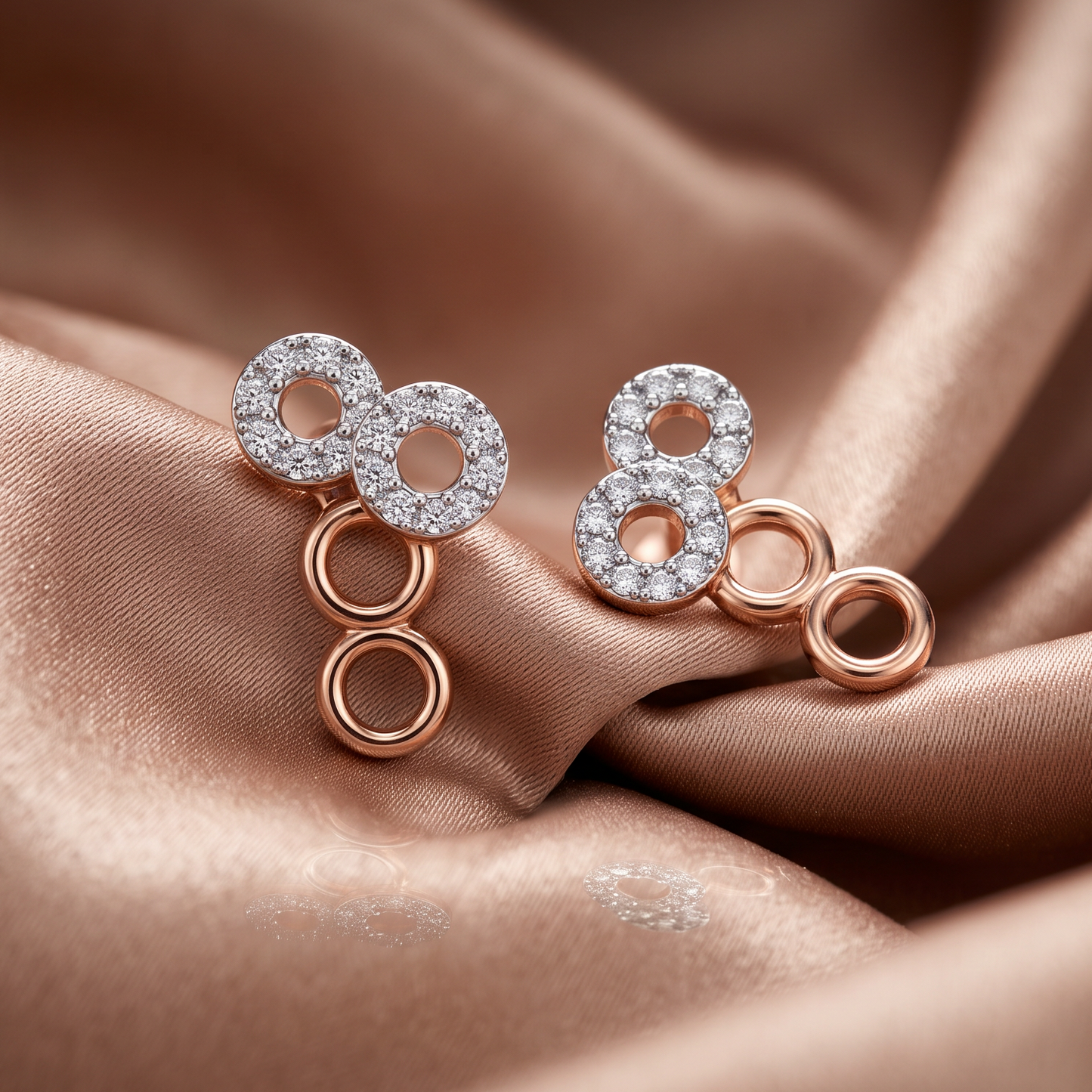 A pair of rose gold earrings with clear pavé-set circular stones and dangling open circular links, displayed on draped champagne satin fabric.