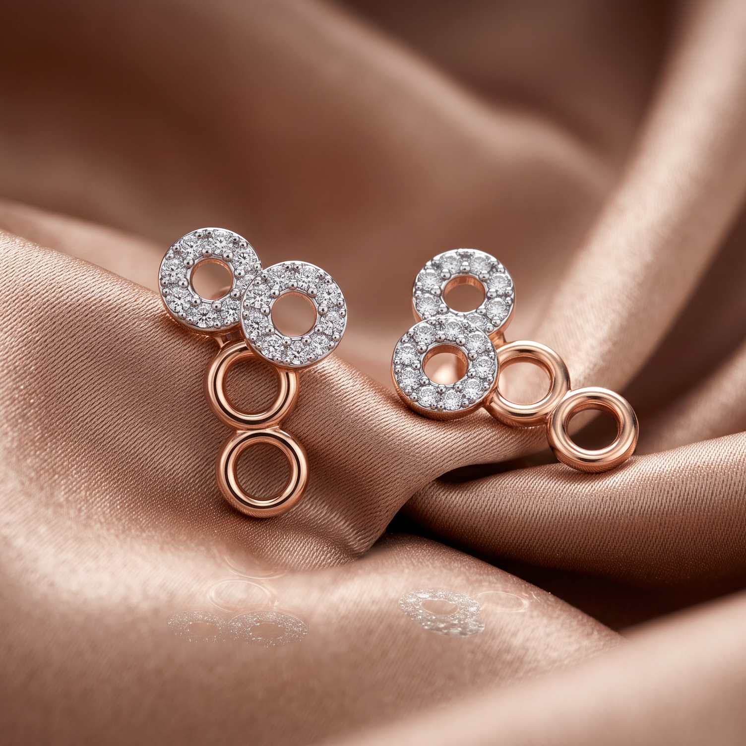 A pair of rose gold earrings with clear pavé-set circular stones and dangling open circular links, displayed on draped champagne satin fabric.